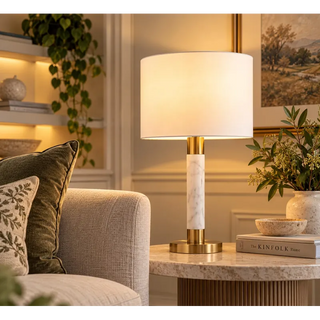 Raffle table lamp lit on stone topped fluted pedestal beside cream sofa
