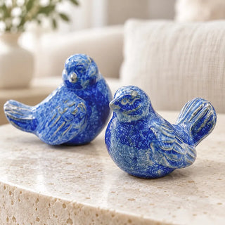 Set of 2 happy blue bird ornaments close up on travertine coffee table by cream sofa